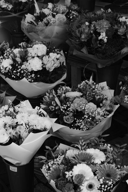 A collection of floral arrangements featuring a variety of fresh flowers, including roses, carnations, daisies, and baby's breath, wrapped in decorative tissue paper and placed in black plastic vases 