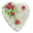 A tender heart-shaped tribute crafted entirely from a dense carpet of small, pristine white chrysanthemums sits against a crisp white background, the surface so closely set it reads like soft, clouded linen. The chrysanthemums' tightly ruffled petals create a cushioned texture that suggests quiet comfort and purity; in soft overhead light their tiny shadows give the heart gentle depth. From the upper left a concentrated cluster of three deep crimson roses offers a striking counterpoint - each rose fully opened, its velvety petals curling outward and releasing the suggestion of a warm, familiar fragrance. Those three roses are cradled in dark glossy foliage and airy, fern-like fronds, with slender blades of bright green bear grass arcing away to draw the eye. Two single red roses punctuate the composition: one nestled near the right curve of the heart and the other planted toward the bottom point, each given a few small green leaves and minimal white filler so the red blooms can speak plainly. The whole shape is neatly traced by a slim emerald-green satin ribbon that frames the perimeter with a refined, solemn edge. The palette of pure white, lush greens and deep red reads as a classic expression of remembrance - purity, respect and enduring love - and the piece feels hand-assembled by a careful florist who understands the hush of a service. For neighbours in Raynes Park and nearby Wimbledon, this quiet, traditional memorial heart conveys solace and a steady, gentle regard for the life being honoured.