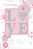 In this detailed image of an anniversary card, the design centres around a soft celebration of enduring romance, presented in a palette of pastel pinks and cool silvery greys that would suit a refined Raynes Park living room. The main focus is the word LOVE arranged in tall, elegant letters across the middle of the card, each one raised and coated with a fine layer of glitter that gives a gentle sparkle without overwhelming the eye. The letter O is replaced by a shimmering silver heart, slightly embossed so it stands out both visually and to the touch, like a polished keepsake. Around this focal word, delicate blossoms in blush, mauve, and soft white unfurl with a watercolour softness, their edges feathered and their centres hinted at with tiny, precise strokes. Fine lines curl into swirling vines and subtle flourishes, evoking the grace of an English spring garden similar to the borders you might stroll past near Cannon Hill Common. Scattered among the flowers are small butterflies and petal-like shapes, adding a sense of gentle motion, as though the design were drifting on a light breeze. Above and below, in an understated, flowing script, the phrases On Our Anniversary and I love you today and always are printed, their spacing carefully balanced with the floral artwork. The overall composition feels tender and intimate, like a card chosen with care from a local Raynes Park florist, echoing the quiet joy of marking another year together with soft, heartfelt sentiment.